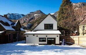 Une maison à deux étages avec un toit en pente, un garage et une cour enneigée.
