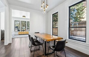 Un espace repas avec une table en bois, des chaises noires et de grandes fenêtres.