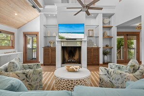 A spacious living room with a fireplace, a ceiling fan, and a large TV screen. - Coastal Beauty - Canal Front, Dock, Pool, Spa, Game Room by Anna Maria Life Vacation Rentals (Anna Maria)