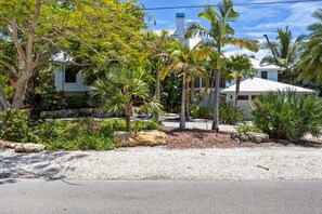 A residential property with a white house, palm trees, and a gravel driveway. - Coastal Beauty - Canal Front, Dock, Pool, Spa, Game Room by Anna Maria Life Vacation Rentals (Anna Maria)