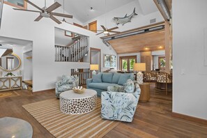 A spacious living area with a staircase, a blue sofa, a round coffee table, and a ceiling fan. - Coastal Beauty - Canal Front, Dock, Pool, Spa, Game Room by Anna Maria Life Vacation Rentals (Anna Maria)