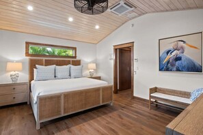 Ein Schlafzimmer mit einem großen Bett, Nachttischen, einer Bank, einem Fenster mit Blick und einer Tür zu einem anderen Raum.