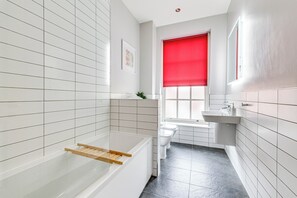 A modern bathroom with white tiled walls, a bathtub with a wooden shelf, a toilet, and a sink. - Spacious 5 -bed Georgian Townhouse I 4 bathrooms I Walk to Liverpool one. (Liverpool)