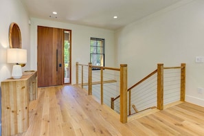 Escada de madeira com guarda-corpo de vidro que leva a um quarto com porta de madeira e janela.