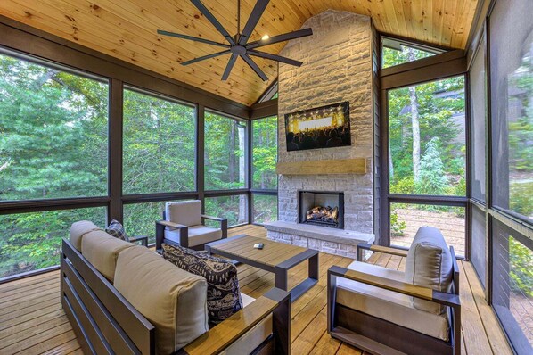 Ein gemütliches Interieur mit Kamin aus Stein, Holzboden und großen Fenstern mit Blick auf den Wald.