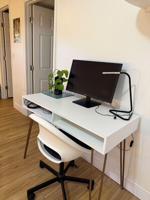 Un escritorio blanco con un monitor de ordenador, teclado y una planta.