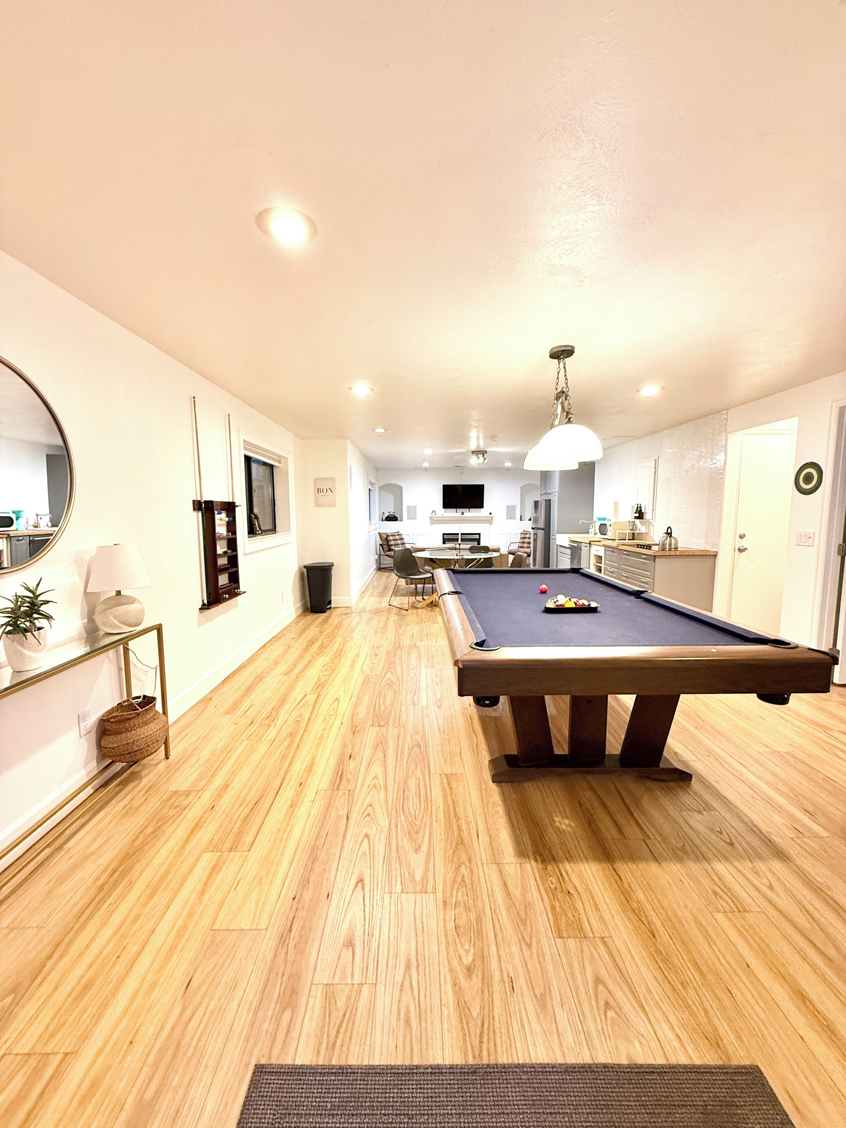 Una mesa de billar en una habitación con piso de madera, un espejo y un televisor en la pared.