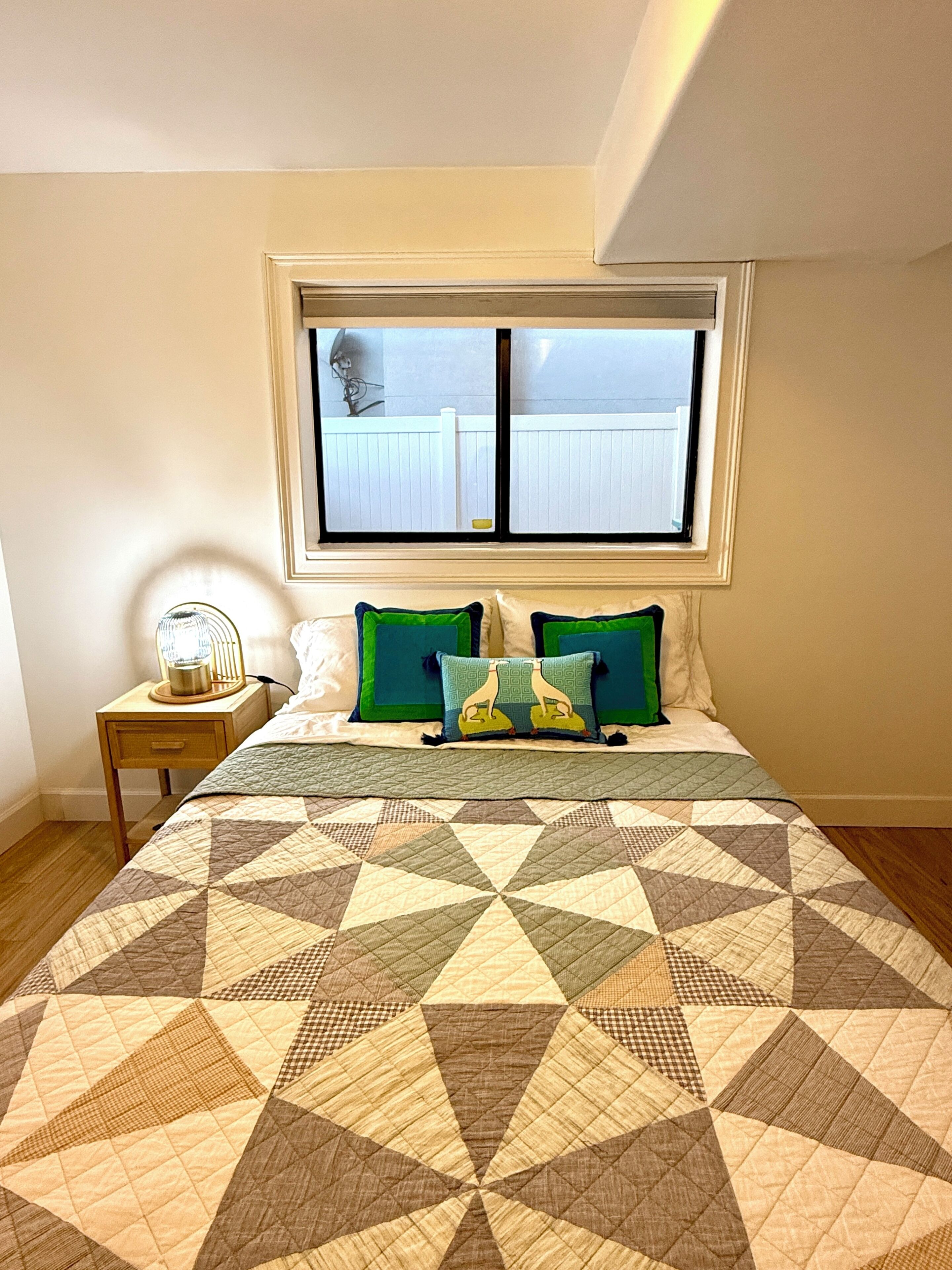 A bedroom with a bed, a window, a bedside table, and a lamp.