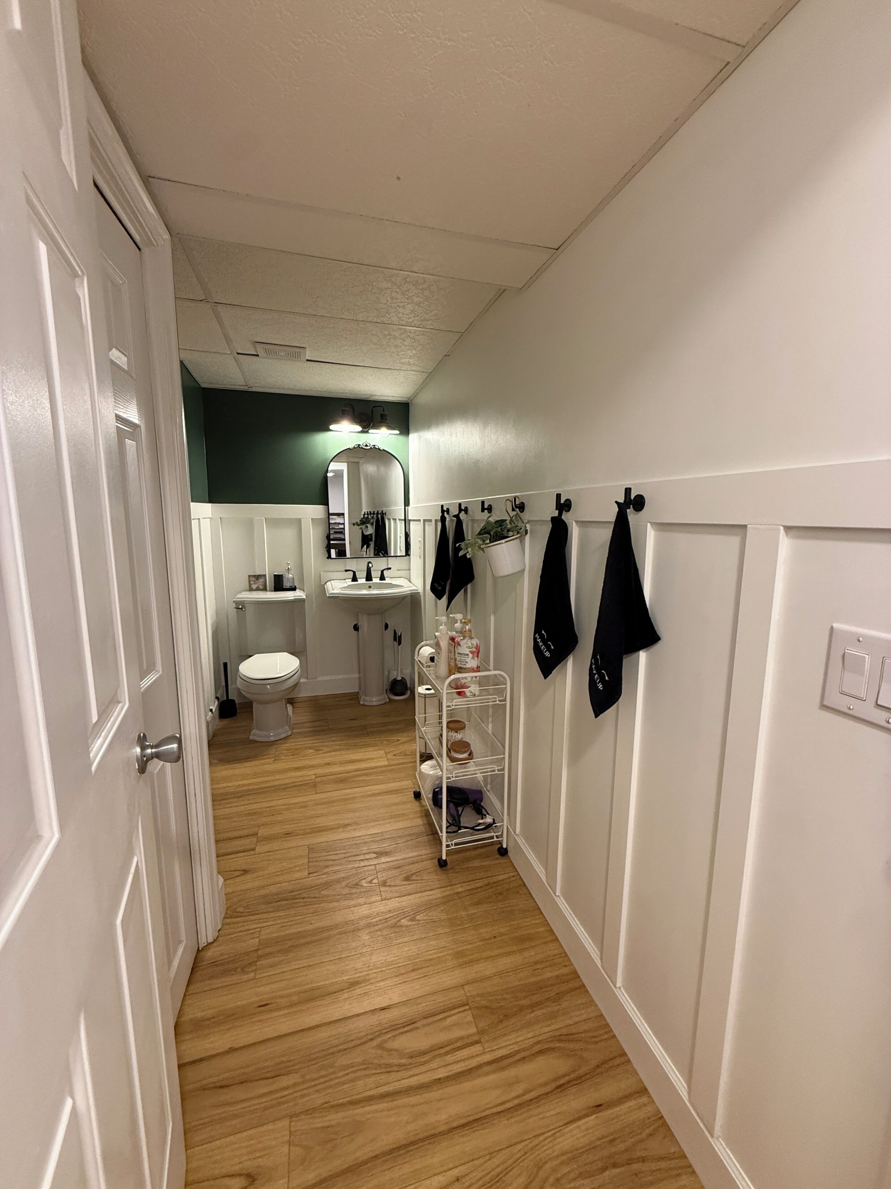 A hallway with a white door, a white sink, a toilet, and a mirror.