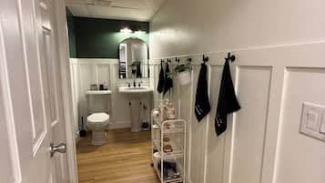 A hallway with a white door, a white sink, a toilet, and a mirror.