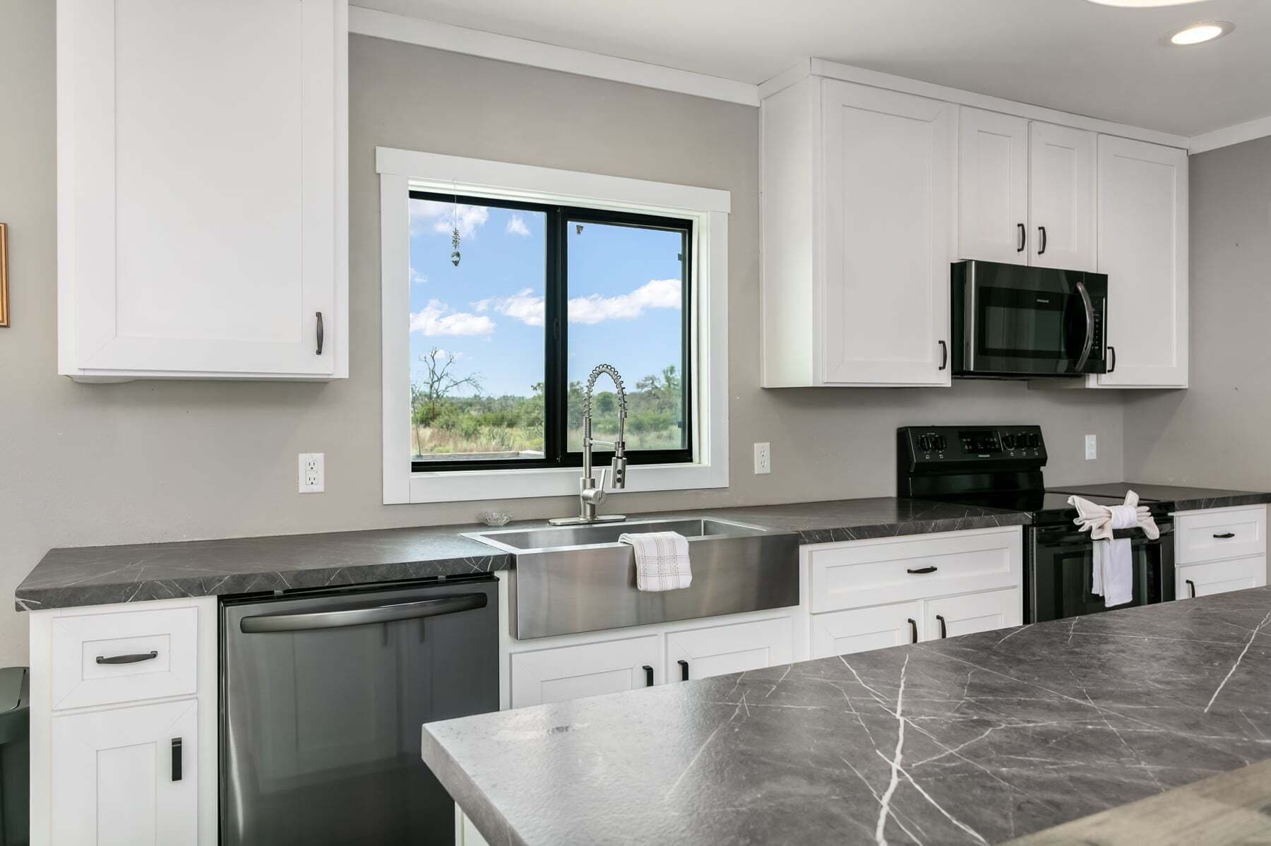 A modern kitchen with white cabinetry, a stainless steel sink, a black microwave, and a dishwasher.