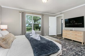 A bedroom with a bed, a television, a dresser, and a view of the outdoors.