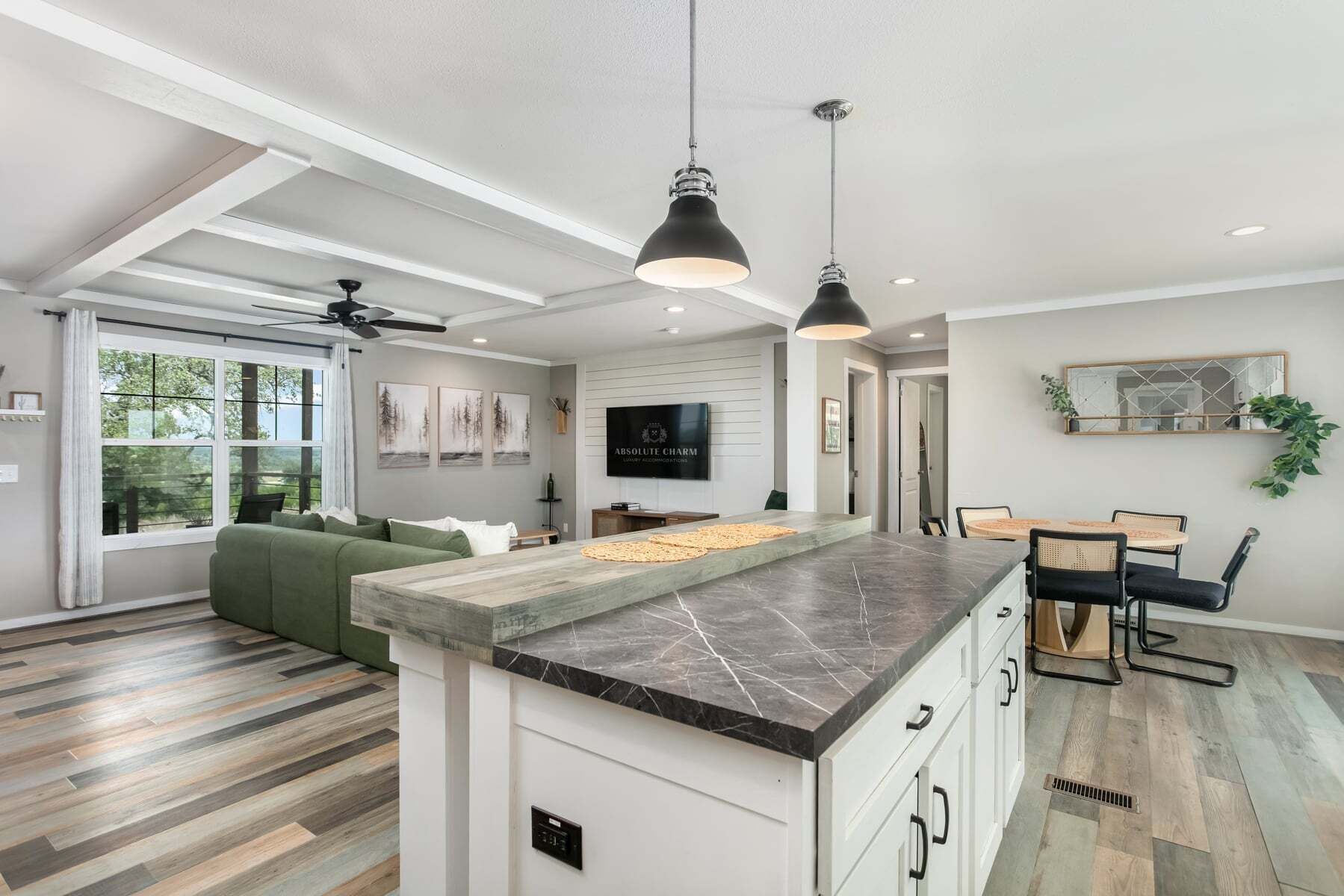 A modern kitchen with a marble countertop, a dining area with a round table and chairs, and a living room with a green sofa.