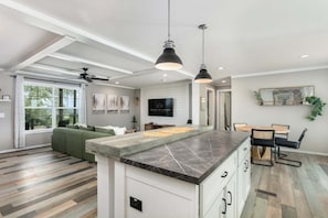 A modern kitchen with a marble countertop, a dining area with a round table and chairs, and a living room with a green sofa. - 3/2 Pet friendly w/ fee Hill Country home w/ hot tub, fire-pit, views & more (Fredericksburg)