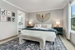 A bedroom with a large bed, bedside tables, a wall-mounted light fixture, and a patterned rug. - 3/2 Pet friendly w/ fee Hill Country home w/ hot tub, fire-pit, views & more (Fredericksburg)