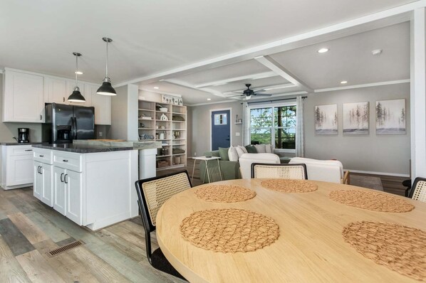 A modern kitchen with white cabinetry, a black refrigerator, and a dining area with a round table and woven placemats.