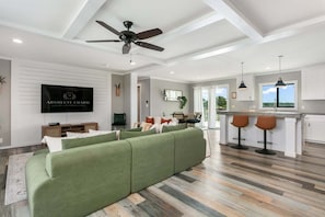 Ein modernes Wohnzimmer mit einem grünen Sofa, einem Deckenventilator und einer Küchenzeile mit Barhocker.