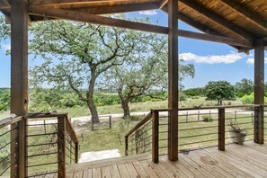 A wooden deck with a railing, overlooking a grassy area with trees.