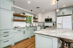 Cozinha moderna com armários verde-claros, bancada de mármore e geladeira de aço inoxidável.