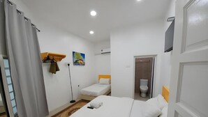 Quarto de hotel com cama, uma cadeira, escrivaninha, quadro e sanita.