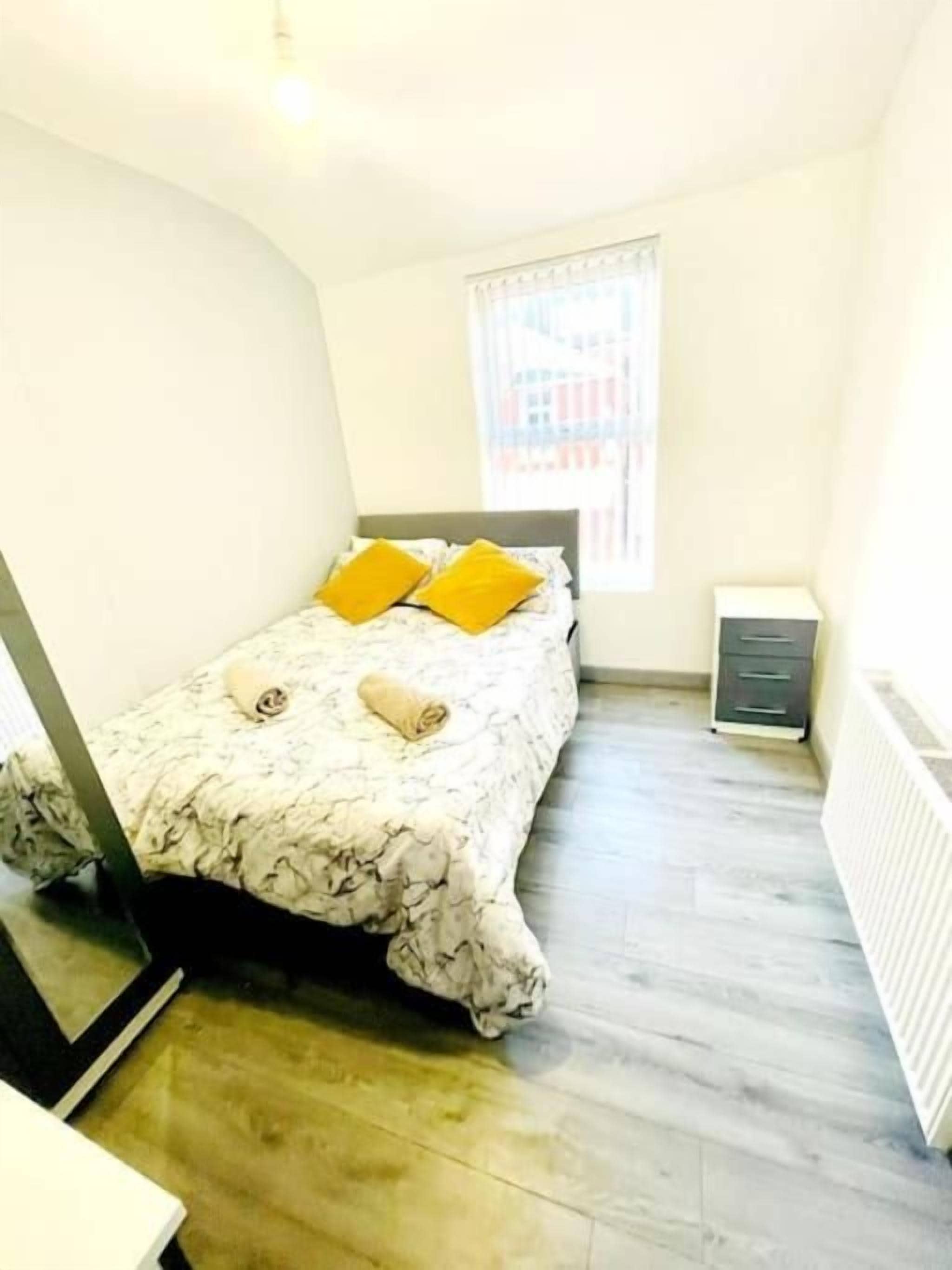 Une chambre à coucher avec un lit, une fenêtre, un radiateur et un petit meuble.