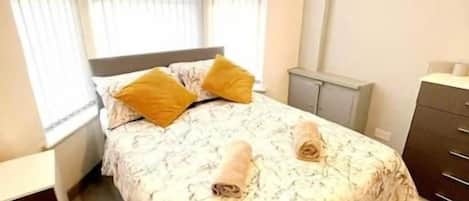 A bedroom with a bed, a nightstand, a dresser, and a window with blinds.