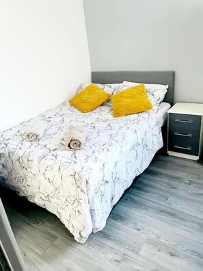 A bed with a marble-patterned bedspread, two pillows, and a nightstand with drawers. - Entrepreneur Stays (Liverpool)