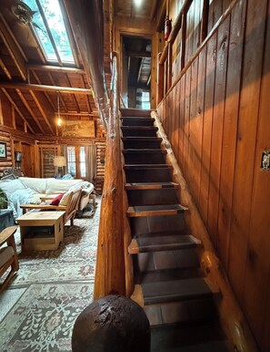 Ein rustikales Blockhaus-Interieur mit Treppe, Holzwänden, einer Couch und einem gemusterten Teppich.
