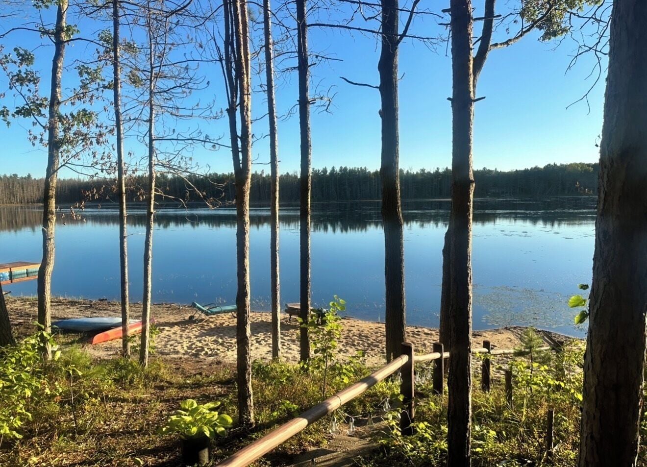 Une vue sur le lac, avec des arbres, une plage de sable et une clôture en bois.