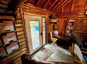 Ein rustikales Blockhaus-Interieur mit Holztür, Bücherregal, Stuhl und Teppich.