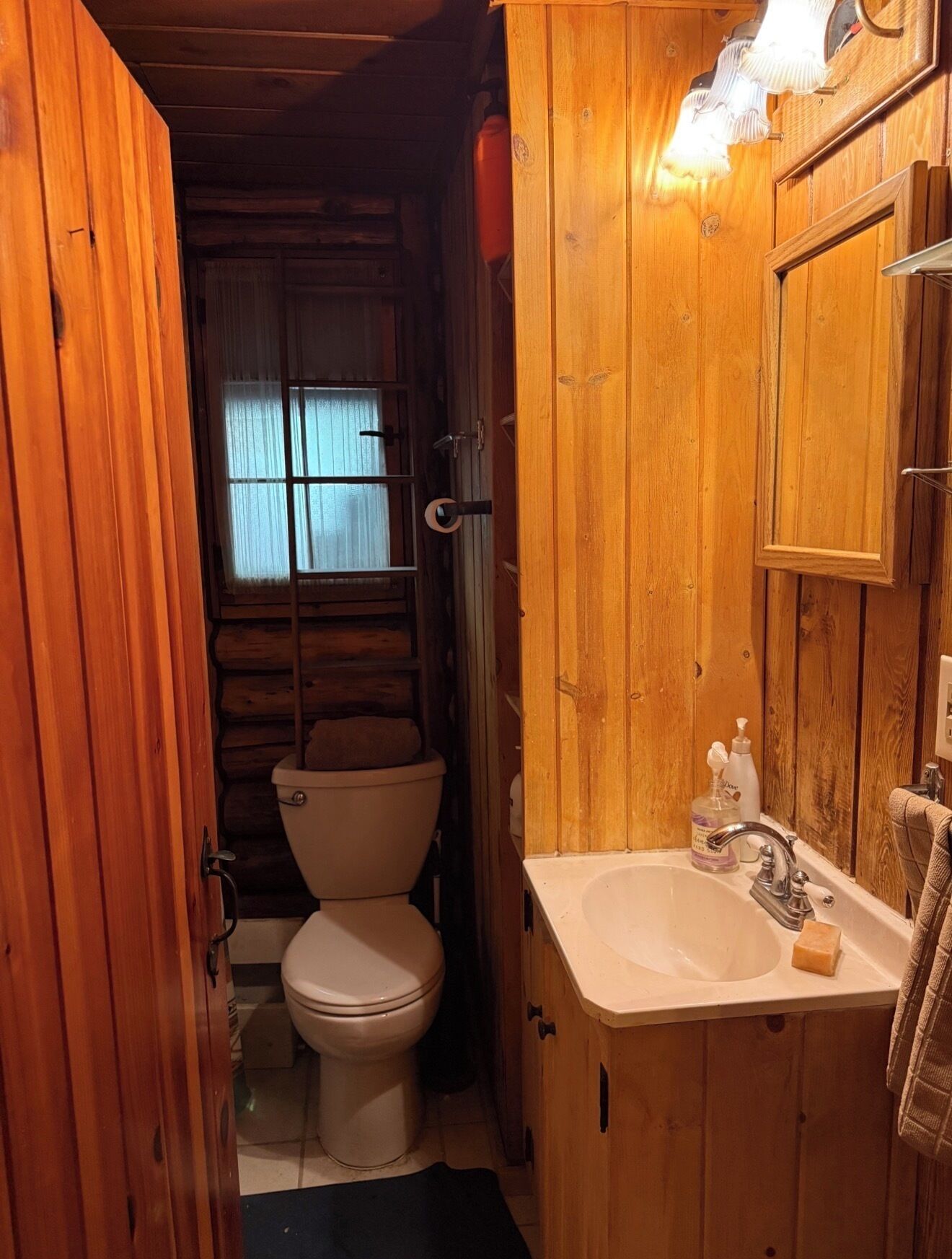 A wooden bathroom with a toilet, sink, and a mirror.