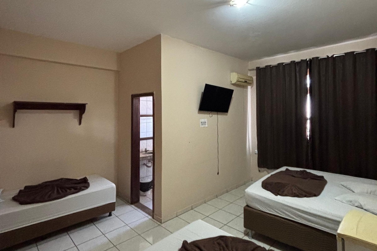A room with two beds, a television mounted on the wall, and a window with curtains.
