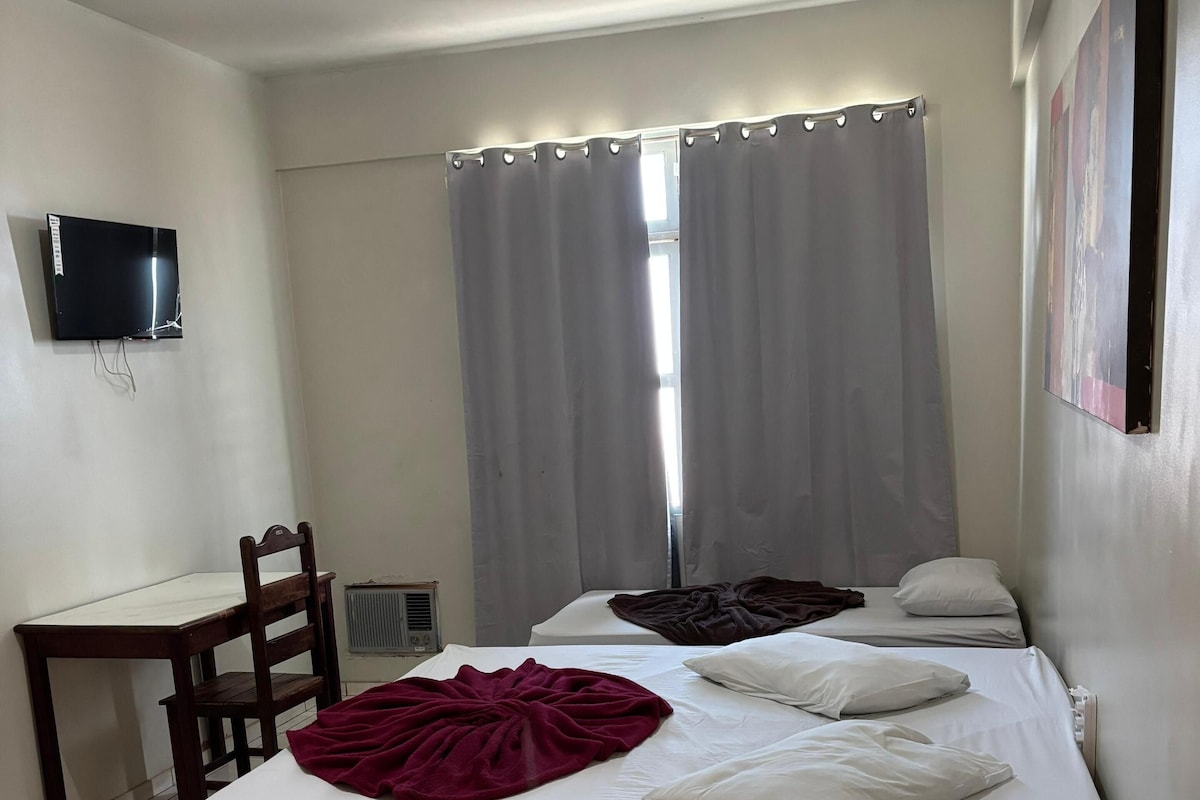A hotel room with a bed, a desk, a chair, a television mounted on the wall, and a window with curtains.