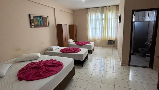 Ein Hotelzimmer mit drei Betten, einem Badezimmer und einem Gang zu einem anderen Zimmer.