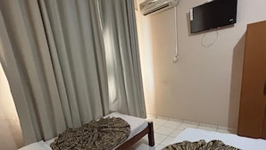Ein Zimmer mit zwei Betten, eines mit einer Zebra-Decke und das andere mit einem schlichten weißen Bettlaken. An der Wand ist ein Fernseher angebracht und darüber befindet sich eine Klimaanlage.