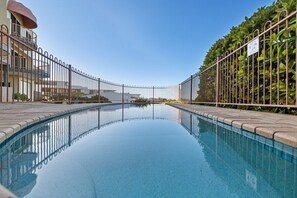 A swimming pool with a clear view of the surrounding area, including a building with a balcony and a fence. - Azure Dreaming - Beachfront Villa @ Coolum Beach (Coolum Beach)