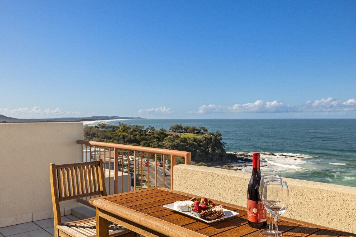 A wooden table with a bottle of wine and a glass, a plate with food, and a view of the ocean.