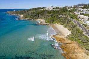 Une zone côtière dotée d’une plage, d’eaux cristallines et d’une route menant à un quartier résidentiel.