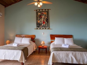 A hotel room with two beds, a ceiling fan, a wall-mounted tapestry, and bedside lamps.
