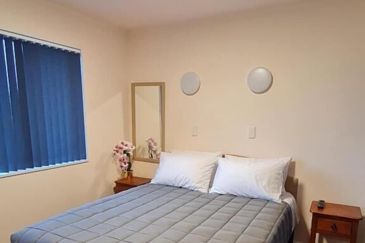 Une chambre d’hôtel standard, équipée d’un lit, d’une table de chevet, d’un miroir et d’une fenêtre avec des rideaux.