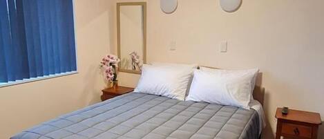 Una habitación estándar de hotel con cama, mesita de noche, espejo y ventana con cortinas.