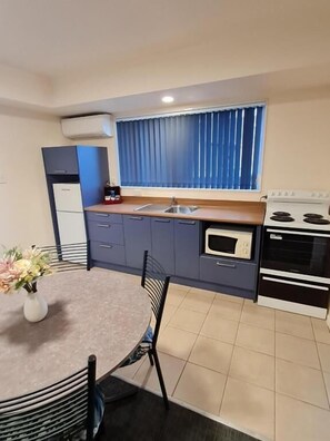 Cocina compacta con mesa, sillas, estufa y ventana con cortinas.