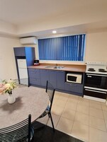A compact kitchen with a dining table, chairs, a stove, and a window with curtains.