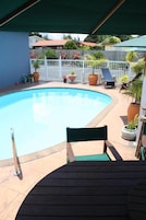 A swimming pool with a wooden deck and a white fence in the background.