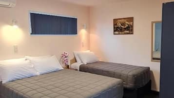 A hotel room with two beds, a small desk, a window with curtains, and a wall-mounted air conditioner.