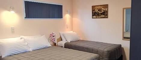 Ein Hotelzimmer mit zwei Betten, einem kleinen Schreibtisch, einem Fenster mit Vorhängen und einer Wand-Klimaanlage.