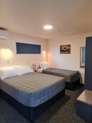 Habitación de hotel con dos camas, un escritorio pequeño, una ventana con cortinas y un aire acondicionado instalado en la pared.