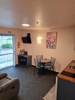 A room with a dining table, chairs, a flat-screen TV, a painting, and a small kitchenette.
