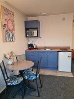 A compact kitchen with a microwave, a small refrigerator, a sink, and a dining area with a table and chairs.