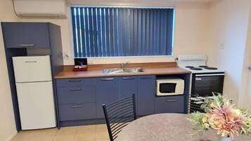 A compact kitchen with a dining area, a built-in oven, and a window with blinds.